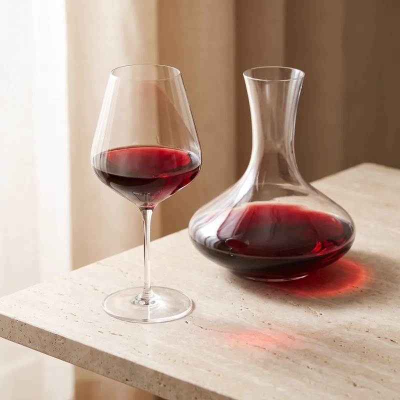 A glass of red wine beside a decanter, catching the light on a stone table.